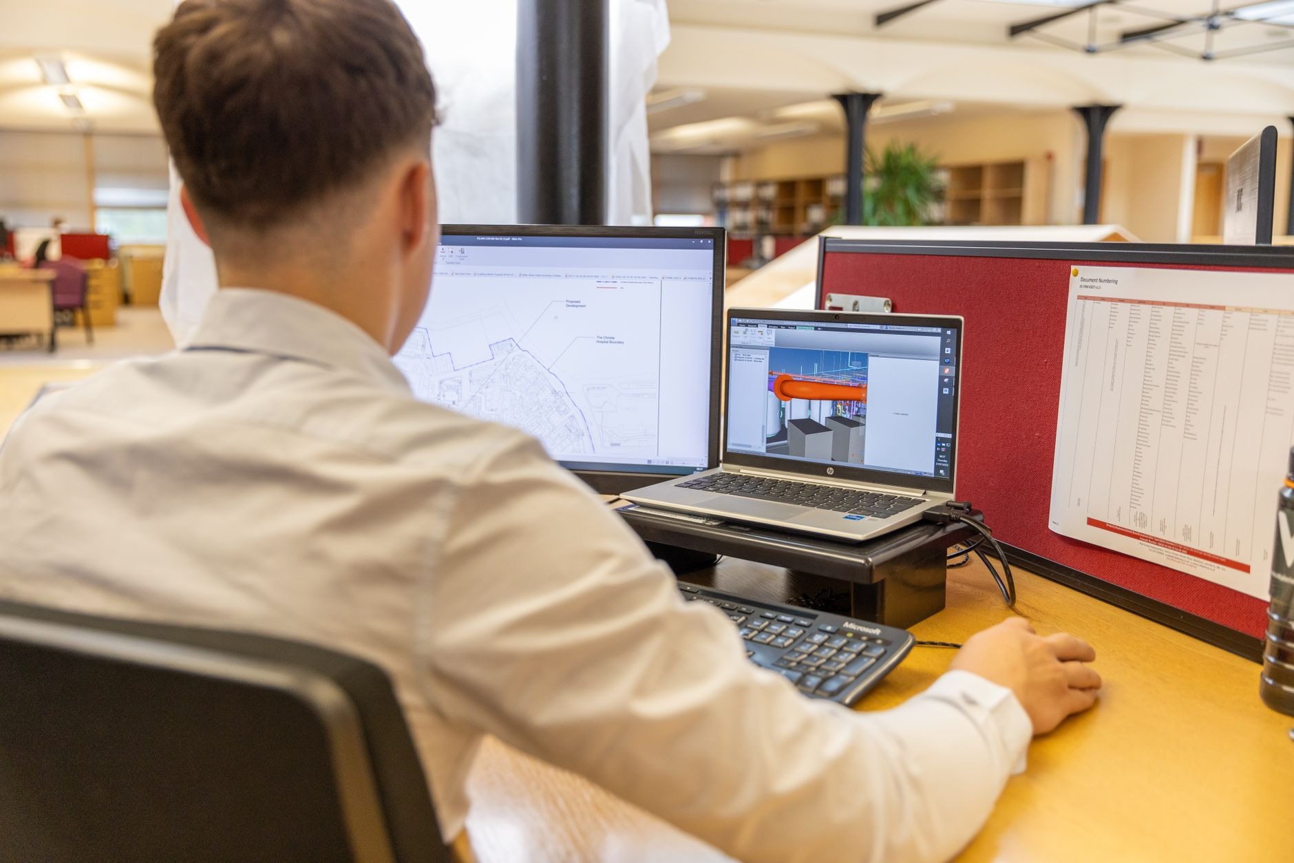 an engineer at a dual-monitor workstation reviewing an AI agent activity log, warm evening office lighting